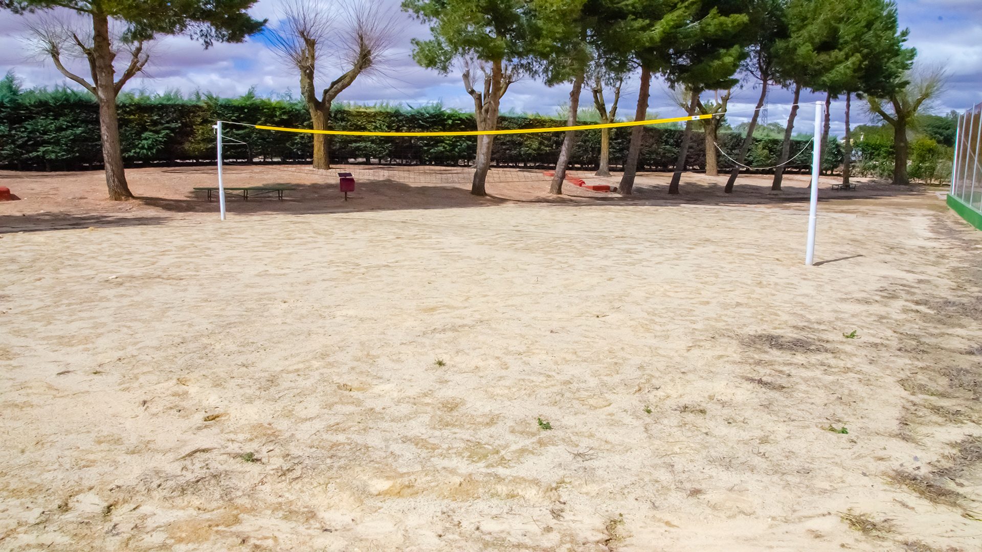 Pista de vóley playa con arena fina, red amarilla y blanca, rodeada por árboles y vegetación en las instalaciones del Club Deportivo y Cultural "Las Tinajas".